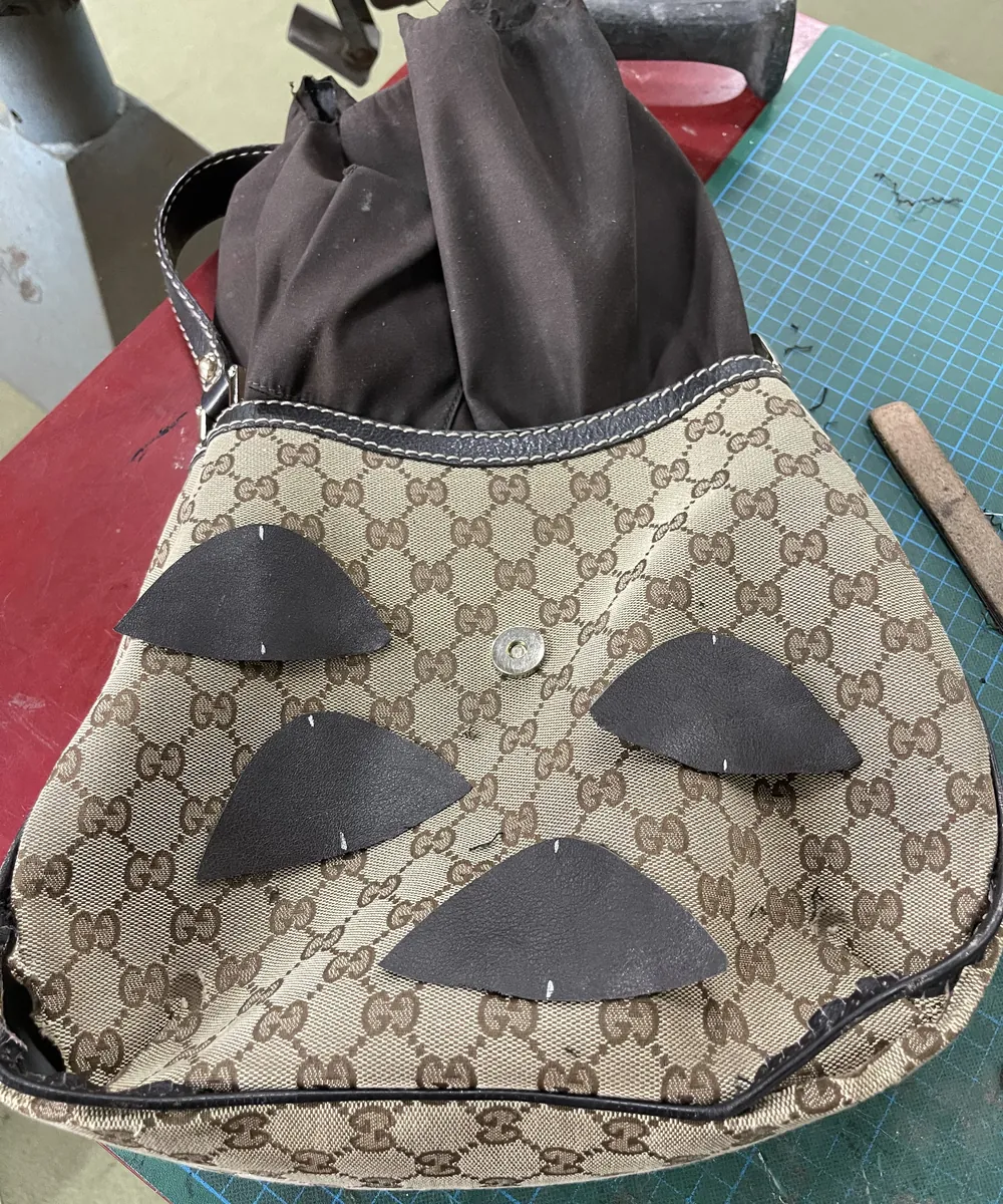 A monogram canvas handbag on the bench with new leather corner patches being fitted