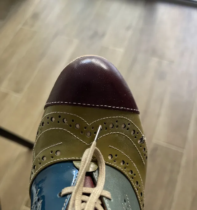 A two-tone brogue in oxblood, olive and teal being re-laced on the bench