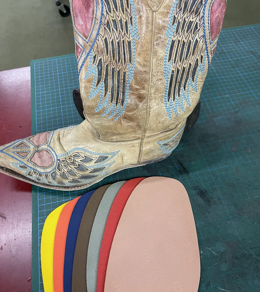 Embroidered western boots beside a fan of coloured heel rubber on the bench