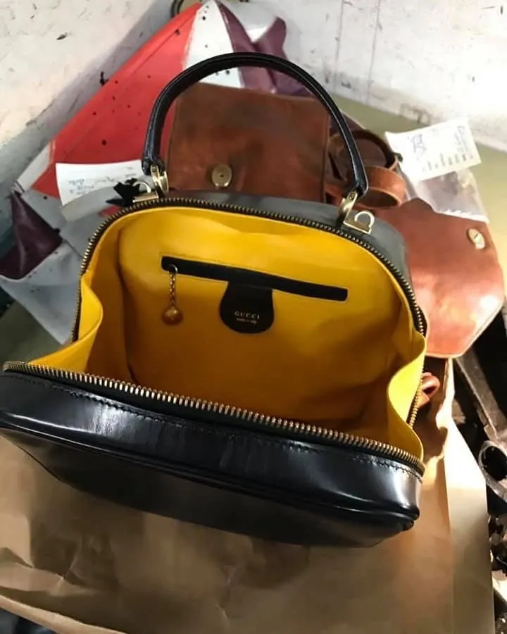 A black leather handbag with a bright yellow lining opened up on the bench among other bags