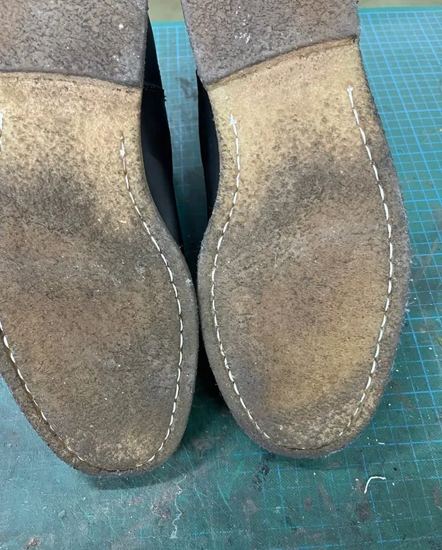 The soles of a pair of desert boots freshly re-stitched in white thread