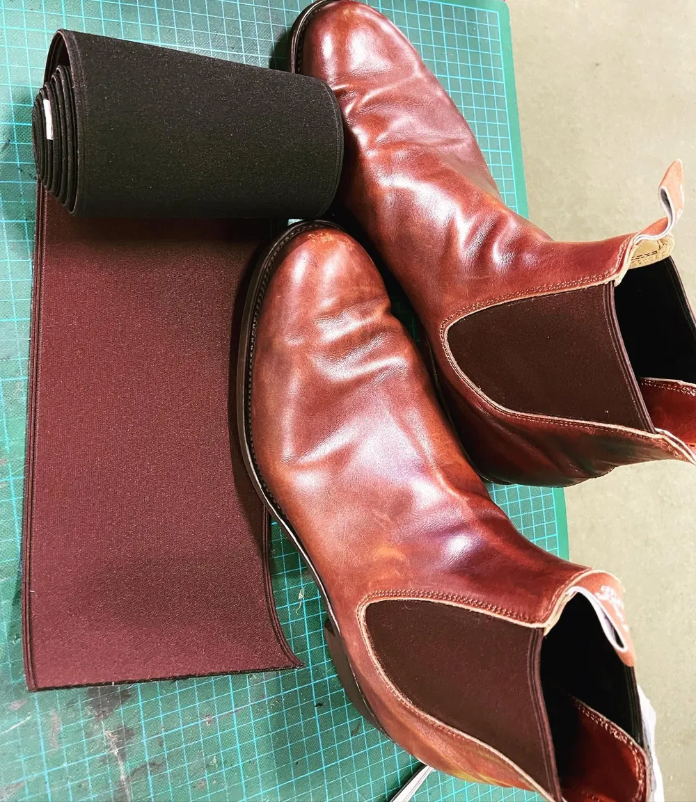 Oxblood RM Williams boots on the cutting mat beside a roll of new elastic for the sides
